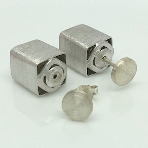 May include: A pair of silver cube earrings with a detailed design. The earrings have a post and a small round back.