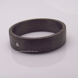 May include: A dark gray ring with a single small diamond set in the center. The ring is made of wood and has a smooth, polished finish.
