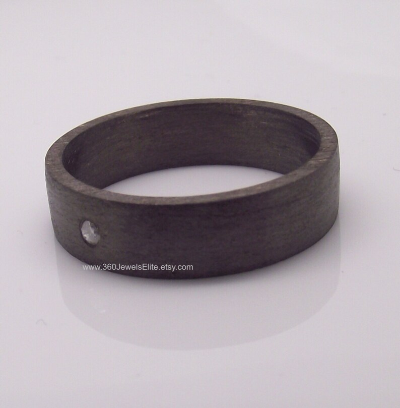 May include: A dark gray ring with a single small diamond set in the center. The ring is made of wood and has a smooth, polished finish.