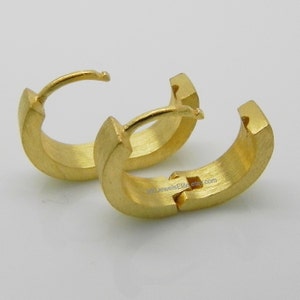 May include: A pair of gold hoop earrings with a brushed finish. The earrings are hinged and have a simple, modern design.