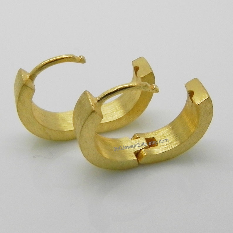May include: A pair of gold hoop earrings with a brushed finish. The earrings are hinged and have a simple, modern design.