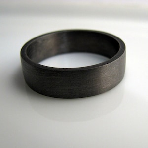 May include: A dark gray, brushed metal ring. The ring is simple and has a flat, wide band.