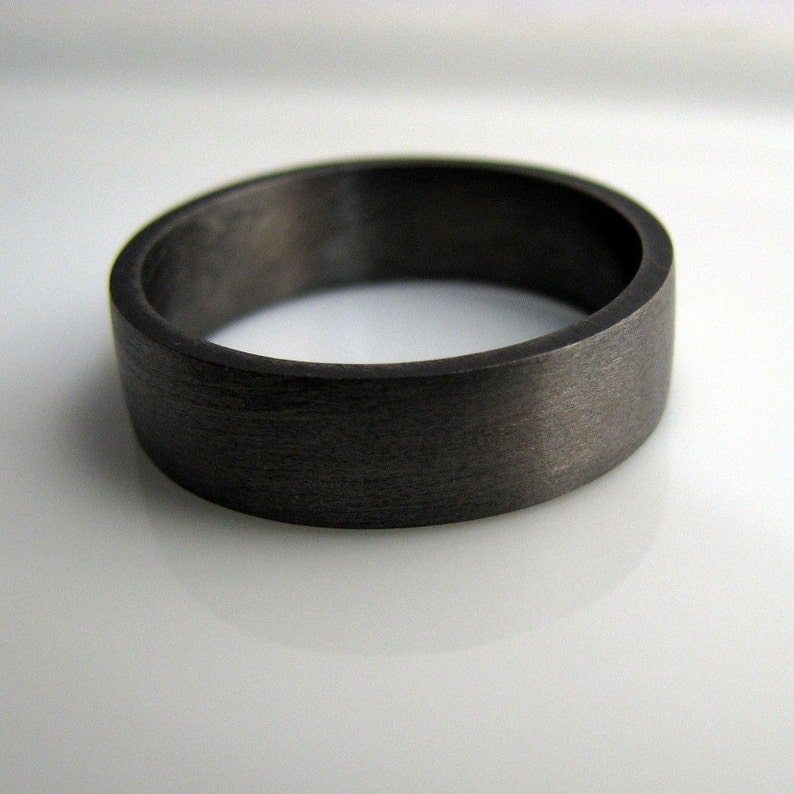 May include: A dark gray, brushed metal ring. The ring is simple and has a flat, wide band.