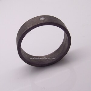 May include: A black carbon fiber ring with a single small diamond set in the center. The ring is shown on a white background. www.360JewelsElite.etsy.com