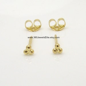 May include: A pair of gold stud earrings with a three-ball design. The earrings are small and delicate, and they would make a great gift for a friend or loved one.