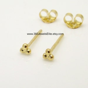 May include: A pair of gold-toned stud earrings with a three-ball design. The earrings are small and delicate, and they would make a great gift for a friend or loved one.