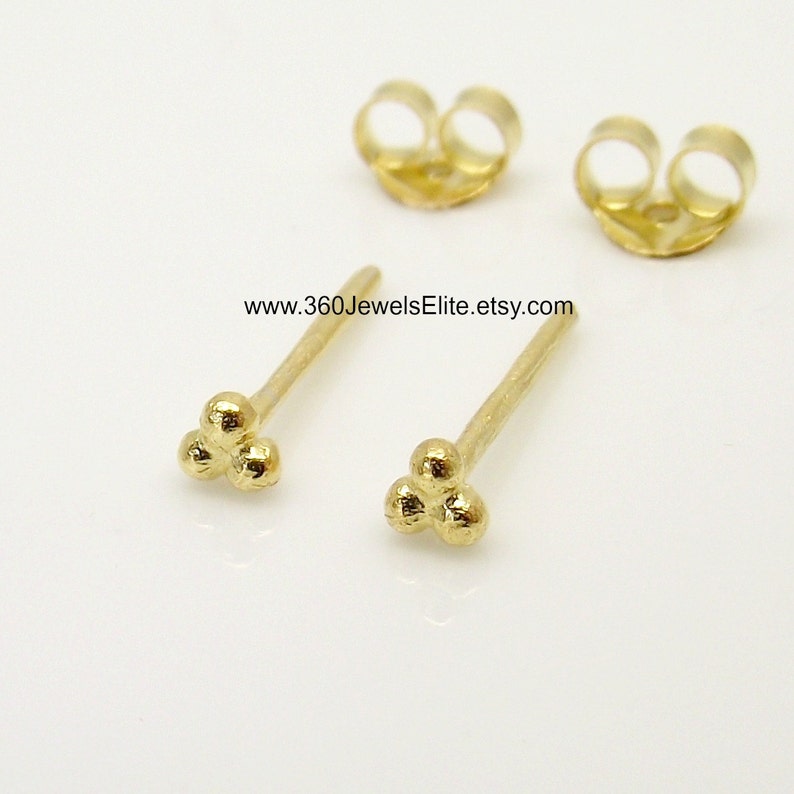 May include: A pair of gold-toned stud earrings with a three-ball design. The earrings are small and delicate, and they would make a great gift for a friend or loved one.