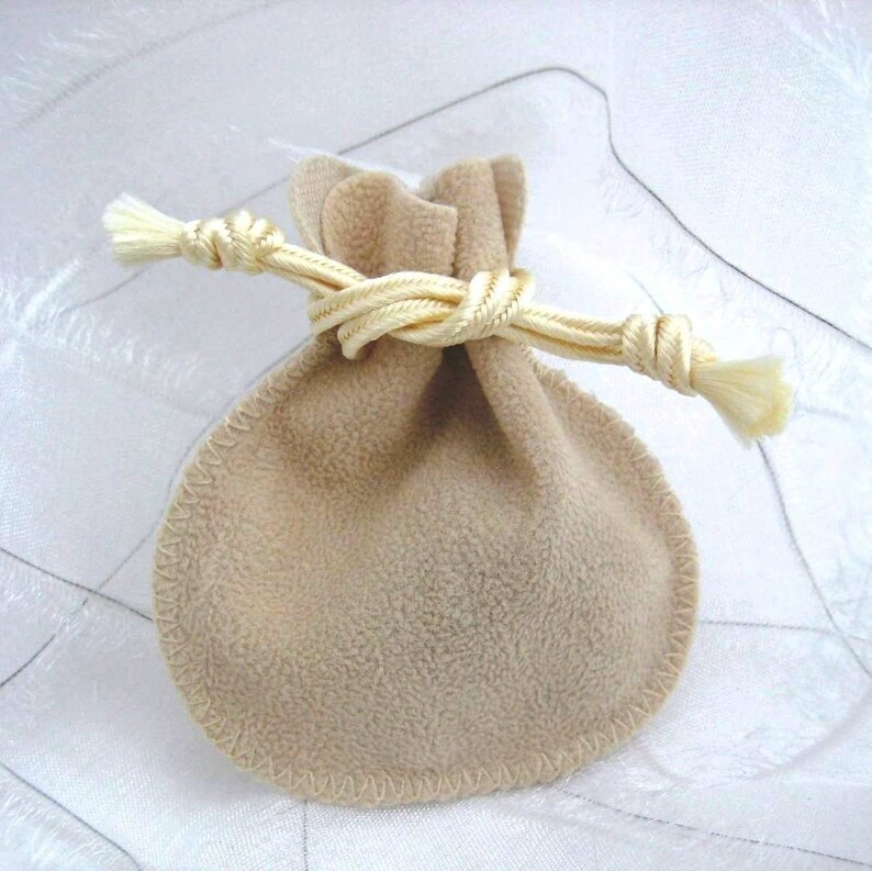 May include: A small, beige drawstring bag made of soft fabric with a cream-colored cord tied in a knot. The bag is perfect for storing small items like jewelry or gifts.