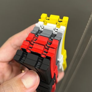 May include: A stack of colorful, interlocking toy blocks. The blocks are in various colors, including black, red, gray, white, and yellow. The blocks are held in place by a hand. The blocks are made of plastic.