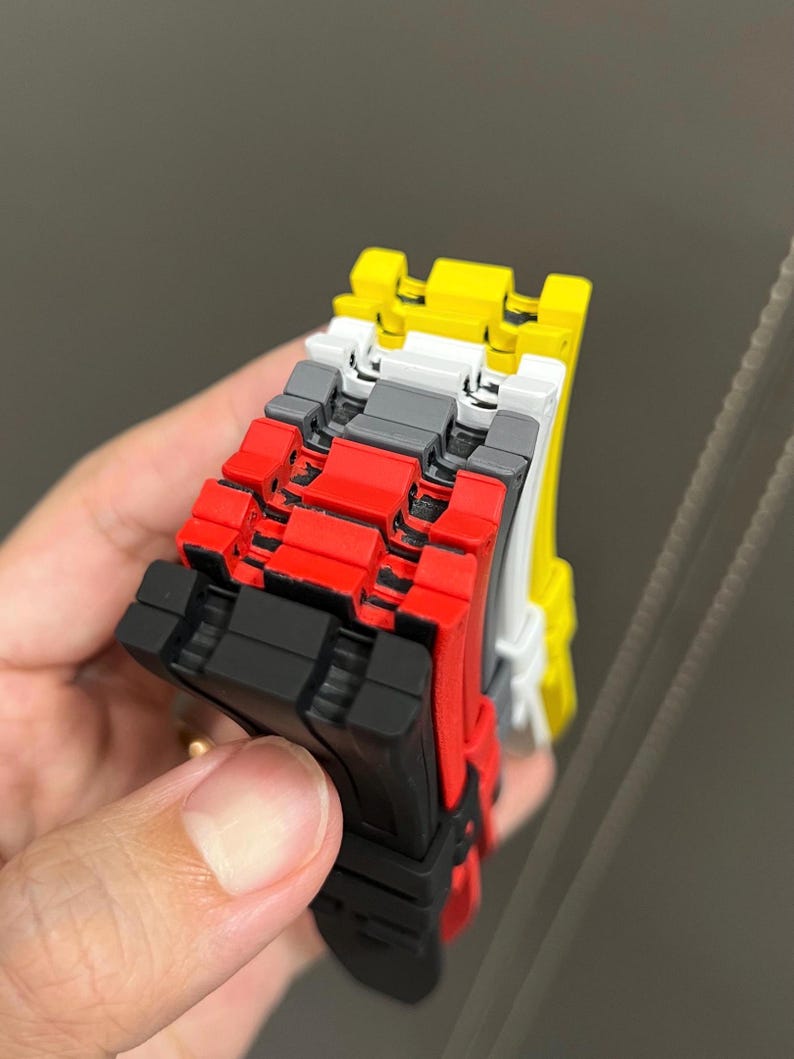 May include: A stack of colorful, interlocking toy blocks. The blocks are in various colors, including black, red, gray, white, and yellow. The blocks are held in place by a hand. The blocks are made of plastic.