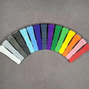 May include: A rainbow assortment of 14 silicone watch straps in various colors, including blue, green, red, orange, yellow, and black. The straps are arranged in a semi-circle, with the darkest colors at the bottom and the lightest colors at the top.