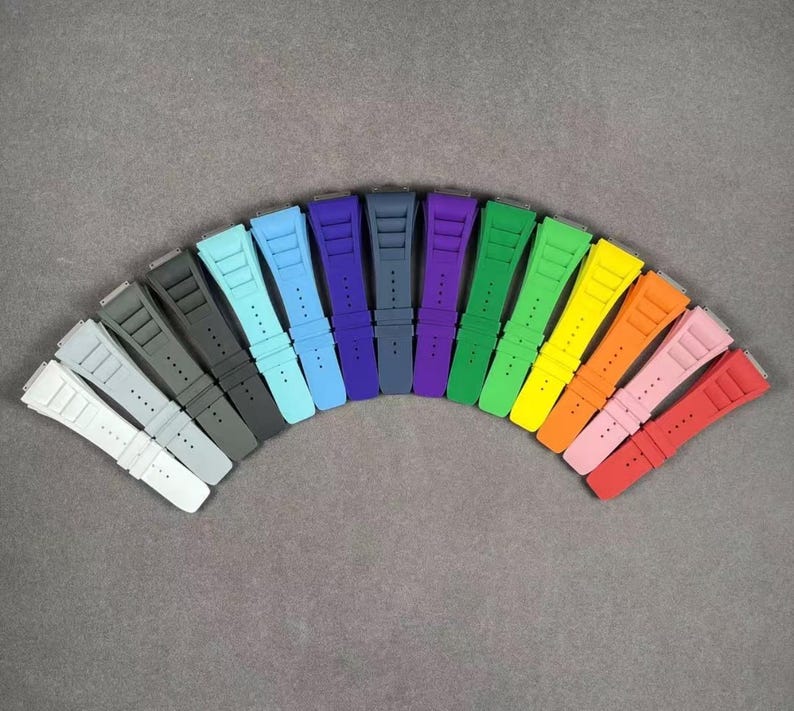 May include: A rainbow assortment of 14 silicone watch straps in various colors, including blue, green, red, orange, yellow, and black. The straps are arranged in a semi-circle, with the darkest colors at the bottom and the lightest colors at the top.