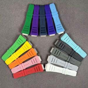 May include: A set of 10 colorful silicone watch bands. The bands are arranged in a semi-circle, with the lighter colors at the top and the darker colors at the bottom. The bands are all the same size and have a smooth, matte finish.
