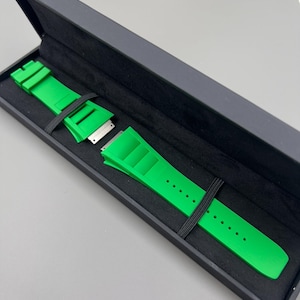 May include: A bright green watch strap in a black box. The strap is made of rubber and has a buckle closure.