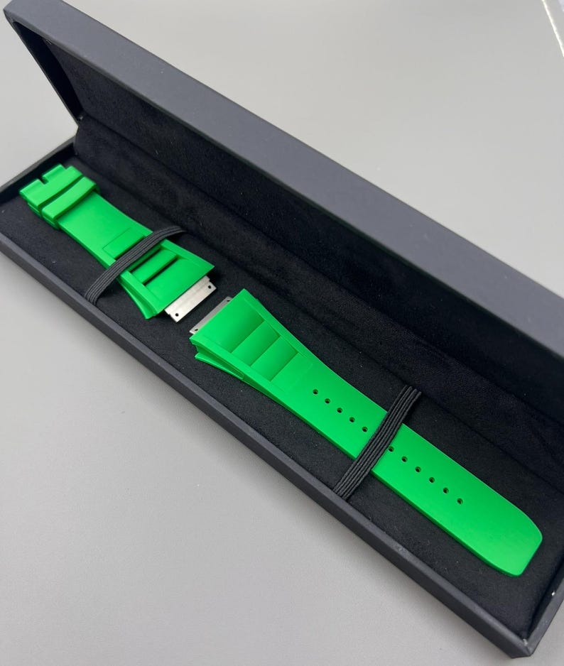 May include: A bright green watch strap in a black box. The strap is made of rubber and has a buckle closure.