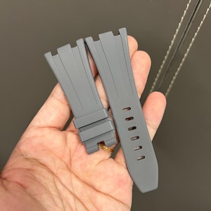 May include: Two gray watch straps. The straps are made of a flexible material and have a textured surface. One strap has several holes for adjustment. The straps are designed to attach to a watch case.