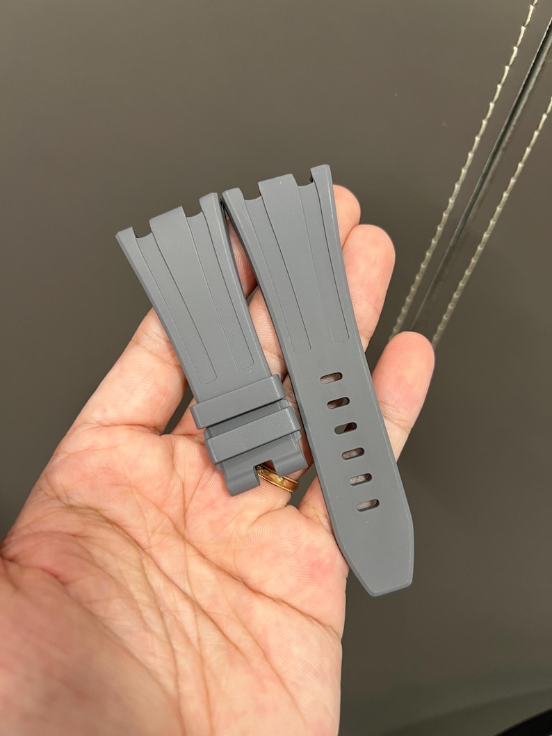 May include: Two gray watch straps. The straps are made of a flexible material and have a textured surface. One strap has several holes for adjustment. The straps are designed to attach to a watch case.