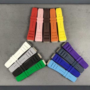 May include: A set of 11 colorful watch bands in various colors, including red, pink, orange, yellow, white, gray, black, green, blue, purple, and dark blue. The bands are made of rubber and have a textured surface.