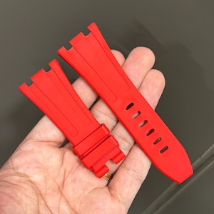 May include: Bright red watch strap. The strap is made of a flexible material and features a series of oval holes for adjustment. The strap is designed to attach to a watch case.