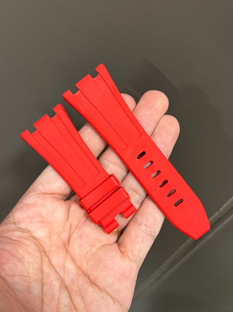 May include: Bright red watch strap. The strap is made of a flexible material and features a series of oval holes for adjustment. The strap is designed to attach to a watch case.