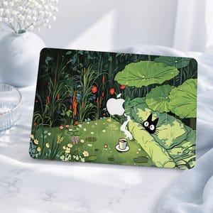 May include: A laptop skin featuring a green garden scene with large lily pads, tall grasses, and red flowers under falling rain. A small black cat with large eyes peeks from behind a leaf near a white cup on a saucer. The Apple logo is visible.