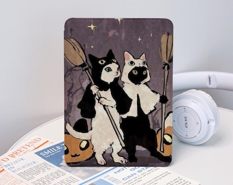 Może przedstawiać: Prostokątne etui na tablet z ilustracją Halloween przedstawiającą dwa koty w kostiumach, trzymające miotły. Koty są czarne i białe, na ciemnofioletowym tle z gwiazdami. Ozdobny i ochronny dodatek.