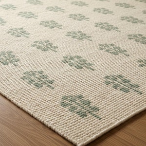 May include: A woven area rug featuring a repeating pattern of sage green leaf motifs set against a cream-colored background. The rug has a textured, looped pile construction with a consistent grid-like arrangement of the botanical shapes throughout.