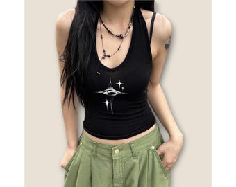 May include: Black tank top with a white graphic of an eye with stars. The tank top is cropped and has a scoop neck.
