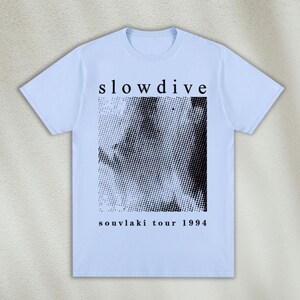 K&ouml;nnte beinhalten: Hellblaues T-Shirt mit einem schwarz-wei&szlig;en Grafikdruck eines Gesichts und dem Text "slowdive souvlaki tour 1994".