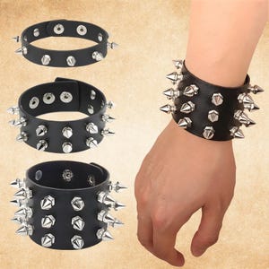 May include: Black leather wristbands with silver spikes. The image shows three wristbands, one worn on a wrist. The wristbands have adjustable closures with multiple snap settings. The spikes are evenly spaced around the bands.