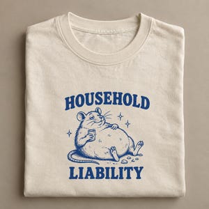 May include: A cream-colored crew neck t-shirt featuring a blue graphic print of a plump rat holding a small can. The text HOUSEHOLD LIABILITY is printed in blue above and below the rat illustration, which is accented by small star shapes.