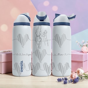 Peut inclure: Trois bouteilles d'eau isolées blanches avec des accents bleus. Chaque bouteille présente un motif en forme de cœur avec un dessin au trait d'une mère et d'un enfant, et les mots "I love you" ou "Mom". La marque "owala" est imprimée sur une bouteille.