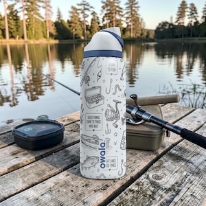 May include: White Owala water bottle with a blue lid and a fishing-themed design. The bottle features illustrations of fishing gear and the phrases "Born to Fish", "Good things come to those who bait", and "Tight lines, good times".