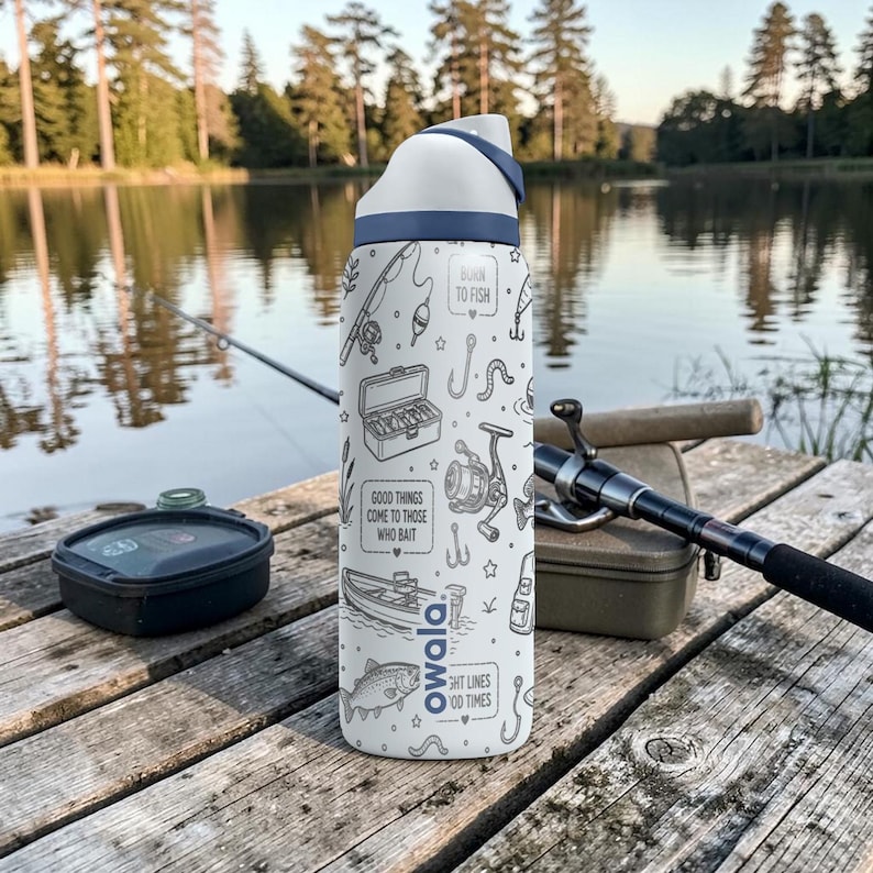 May include: White Owala water bottle with a blue lid and a fishing-themed design. The bottle features illustrations of fishing gear and the phrases "Born to Fish", "Good things come to those who bait", and "Tight lines, good times".