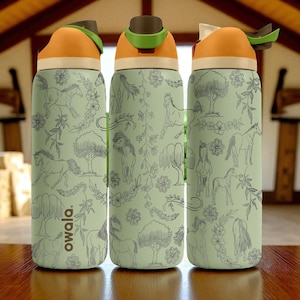 Puede incluir: Tres botellas de agua con un fondo verde claro y un patrón de caballos, árboles y elementos florales. Las botellas tienen tapas naranjas y marrones con un asa verde. La marca "owala" está impresa en el lateral de una botella.
