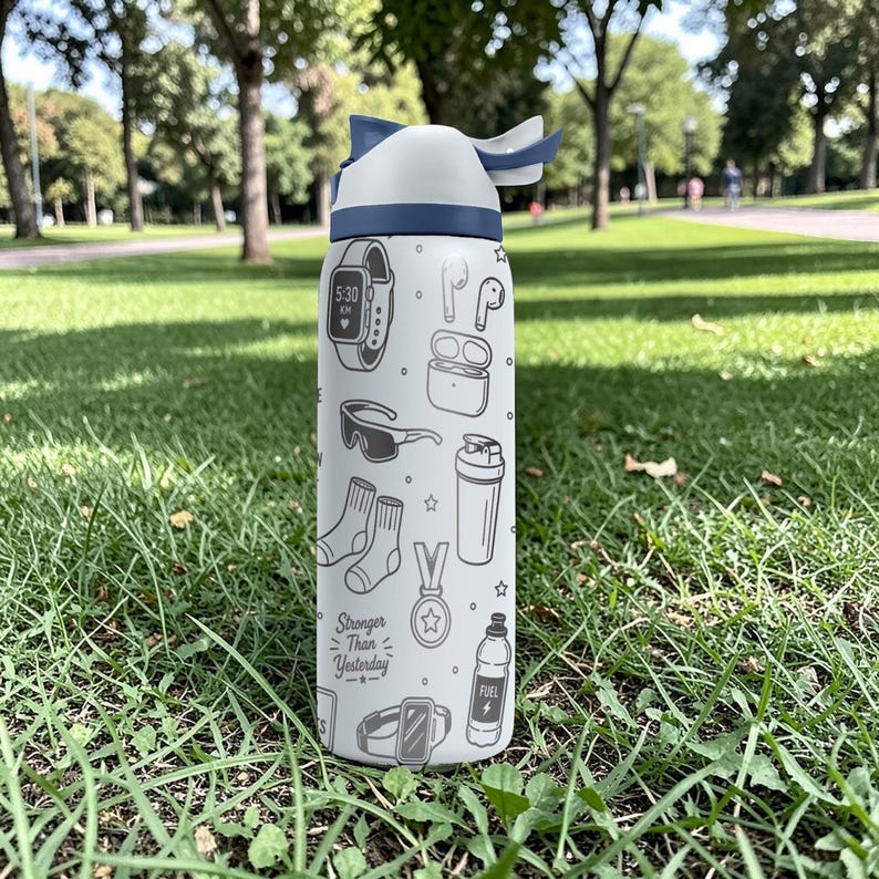 May include: White water bottle with a blue lid and a variety of black and white illustrations, including a smartwatch, sunglasses, and socks. The bottle has the text "Stronger Than Yesterday". The bottle is sitting on green grass.