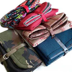 May include: A collection of four folded fabric organizers secured with straps and metal D-rings. The items feature various patterns including a multi-colored floral print, a red dotted texture, a tan plaid, and a green camouflage print.