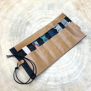 Könnte beinhalten: Eine braune Leder-Uhrenrolle mit sechs Fächern zum Verstauen von Uhrenarmbändern. Die Rolle ist mit schwarzem Filz ausgekleidet und hat einen schwarzen Kordelverschluss.