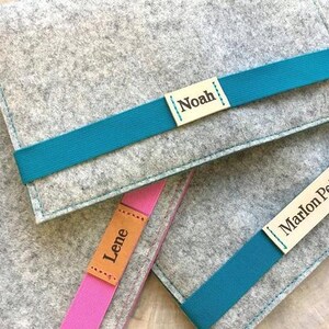 May include: Three gray felt pouches with teal ribbon closures. Each pouch has a personalized leather label with a name: Noah, Lene, and Marlon Petr.