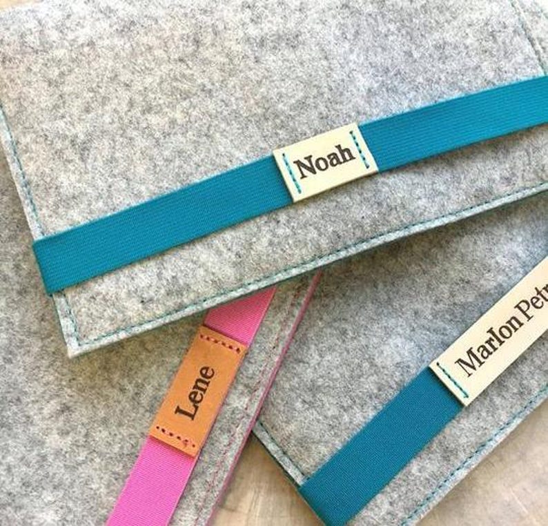 May include: Three gray felt pouches with teal ribbon closures. Each pouch has a personalized leather label with a name: Noah, Lene, and Marlon Petr.
