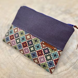 May include: A purple zippered pouch with a colorful geometric pattern on the bottom half. The pouch has a brown leather tag with the text "Handmade with Love" on it.