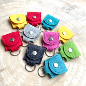Puede incluir: Surtido de llaveros de fieltro en varios colores, incluyendo amarillo, rojo, gris, rosa, azul y verde. Cada llavero tiene un pequeño bolsillo y un anillo de metal.