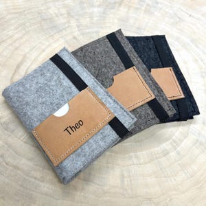 Può includere: Tre pochette in feltro con tasche in pelle. La pochette anteriore ha il nome "Theo" scritto sulla tasca in pelle.