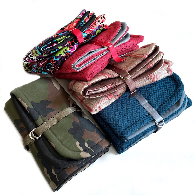 May include: A collection of four folded fabric organizers secured with straps and metal D-rings. The items feature various patterns including a multi-colored floral print, a red dotted texture, a tan plaid, and a green camouflage print.