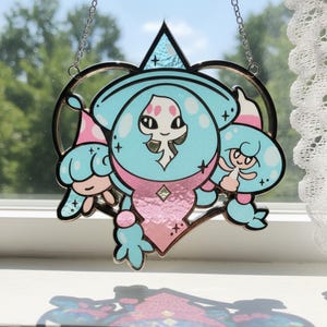 Puede incluir: Un atrapasoles de vidriera con un personaje de dibujos animados en tonos azul claro y rosa. El personaje tiene una cabeza grande y está enmarcado por una forma de corazón. El atrapasoles cuelga de una cadena.