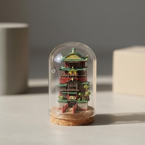 Puede incluir: Un edificio en miniatura de estilo japon&eacute;s, con detalles en rojo, verde y amarillo, est&aacute; encerrado en una c&uacute;pula de cristal. El modelo detallado se asienta sobre una base de corcho. Una peque&ntilde;a bandera es visible. Un objeto decorativo &uacute;nico.