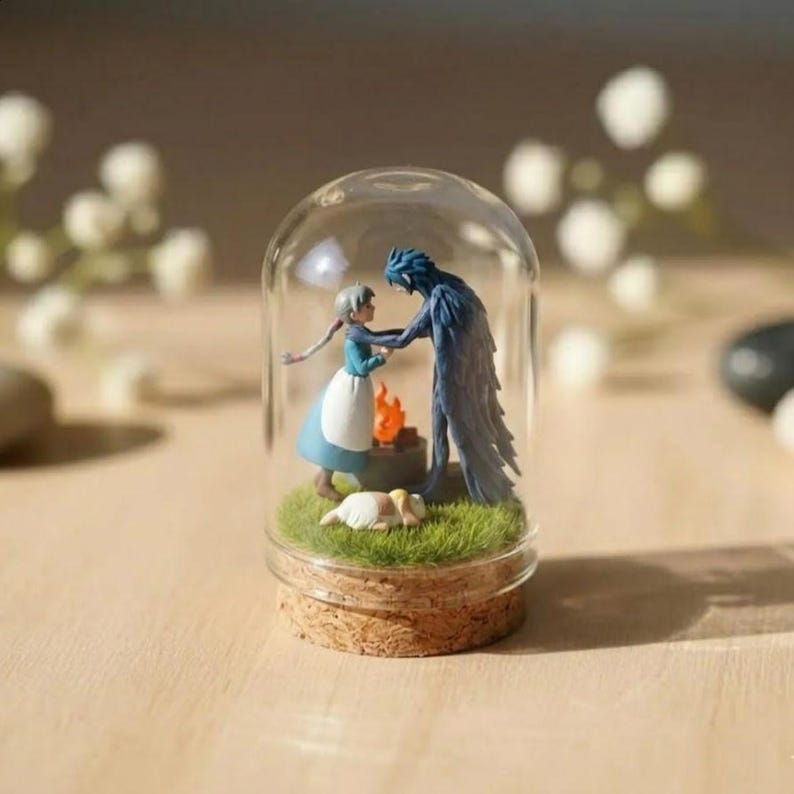 Puede incluir: Un terrario de c&uacute;pula de cristal en miniatura que presenta una escena con dos figuras, un peque&ntilde;o fuego y un perro durmiendo sobre hierba verde. Las figuras son una mujer con un vestido azul y una criatura alada azul. La c&uacute;pula tiene una base de corcho.