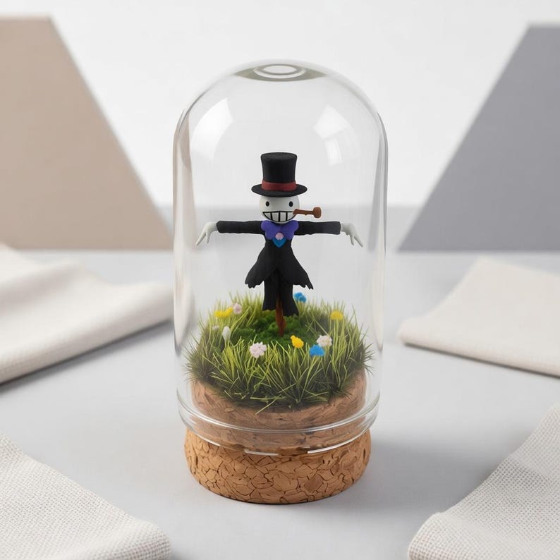 Puede incluir: Una c&uacute;pula de cristal caprichosa con una figura de espantap&aacute;jaros en miniatura con sombrero de copa negro, abrigo y bufanda morada. La figura est&aacute; sobre un lecho de hierba verde con peque&ntilde;as flores, sobre una base de corcho.