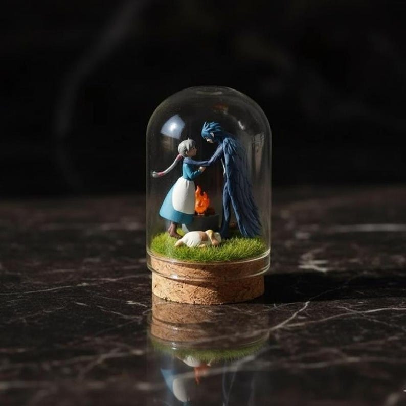 Puede incluir: Un terrario en miniatura con forma de c&uacute;pula de cristal que presenta figuras de dos personajes de una pel&iacute;cula de fantas&iacute;a. La escena incluye un peque&ntilde;o fuego, un perro durmiendo y hierba verde. La c&uacute;pula est&aacute; sobre una base de corcho.