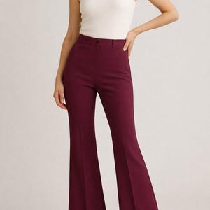 May include: Burgundy high-waisted flared pants with a single button closure. The pants are paired with a white sleeveless top. The pants have a tailored design with a subtle flare from the knee down. The outfit is suitable for various occasions.